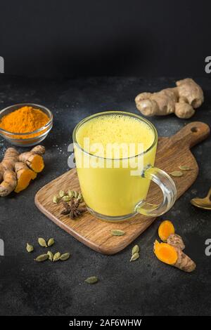 Glass of ayurvedic golden turmeric latte milk with curcuma powder over black table. Vertical shot. Stock Photo