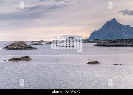 SVOLVAER, NORWAY - July 16 2019: ferryboat sails amid cliff archipelago in fjord out of Arctic touristic little town , shot under bright cloudy light Stock Photo