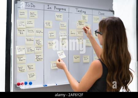 Side View Of Businesswoman Writing On Sticky Notes Attached To White Board In Office Stock Photo
