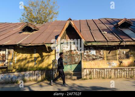 An old crumbling stone house with a textured wooden door, gable and slanted roofs in Almora. A boy walks past on the street outside. Stock Photo