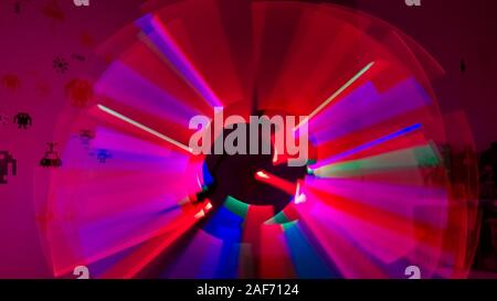 Boy playing in his room with lightsaber in various colors with figures of space invaders on the wall. Lightpaint effect Stock Photo