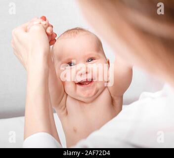 Happy six month baby girl receiving massage therapy in pediatric clinic. Manual therapist manipulates chils's arms Stock Photo