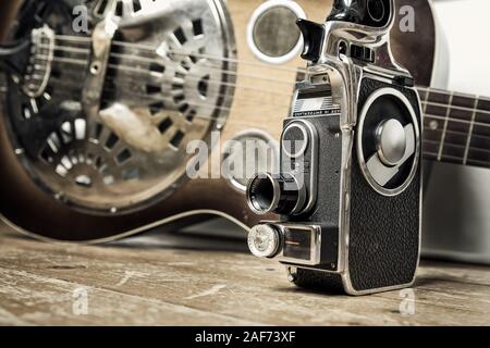 A Vintage film camera is seen on a wooden floor with a Dobro guitar as background Stock Photo