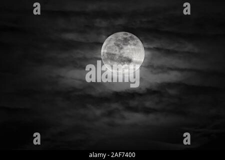 Full Moon shining brightly through dark clouds - black sky Stock Photo