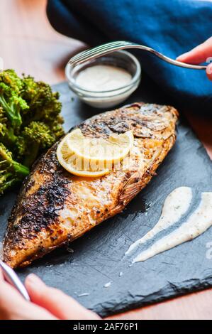 Whole roasted dorado fish with broccoli and sauce on a slate board. Stock Photo