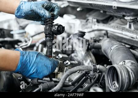 Male specialist's hands in dusty rubber gloves holding new nozzle for car engine in service station. Replacing ignition coil and nozzles of old dirty Stock Photo
