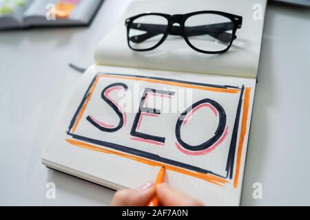 High Angle View Of A Businessperson Writing Search Engine Optimization Concept On Notebook Stock Photo