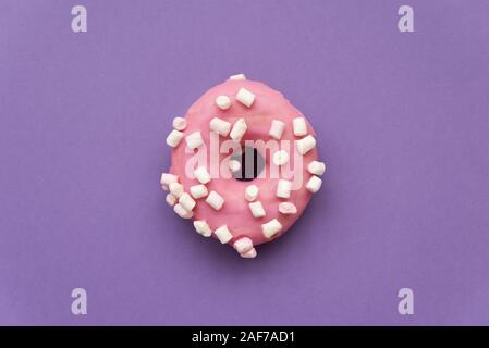 Pink donut decorated marshmallow on purple background. Flat lay. Top view. Unhealthy food Stock Photo