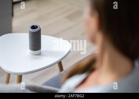 Woman Listening To Black Wireless Speaker On Furniture Stock Photo