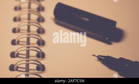 Black pen and cap on blank paper in a spiral notebook, closeup photo. Stock Photo