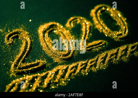 2020 number poured from gold glitters on a dark green background. Stock Photo