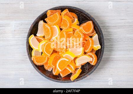 top view of sweet sugar lemon and orange marmalade slices in ceramic bowl on gray wooden board Stock Photo