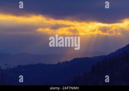 Rays of sunlight shining through clouds over dark landscape in the evening. Faith, religion, hope and nature concepts. Stock Photo