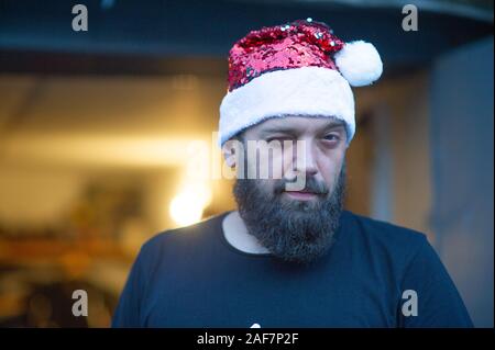 Santa Claus walking on city street. Man with a beard on the street in the summer in a hat of Santa Claus. A man with an emotional beard poses on a bac Stock Photo