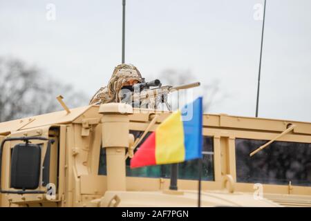 BUCHAREST, ROMANIA - December 1, 2019: Romanian army sniper dressed in a ghillie suit holds a M110 sniper rifle on top of a Humvee armored vehicle dur Stock Photo