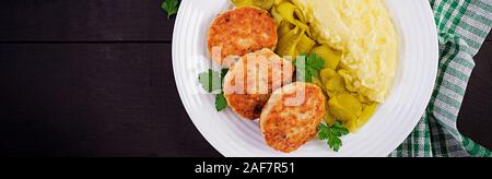 Homemade fried cutlets/meatballs with mashed potatoes and pickled cucumber on white plate. Top view, overhead, banner Stock Photo