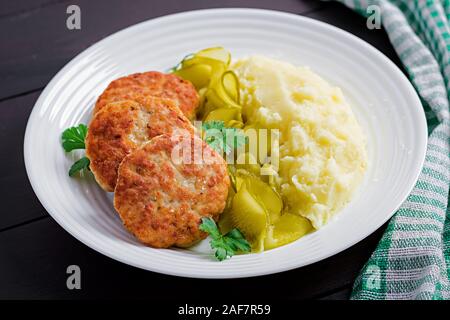Homemade fried cutlets/meatballs with mashed potatoes and pickled cucumber on white plate. Stock Photo