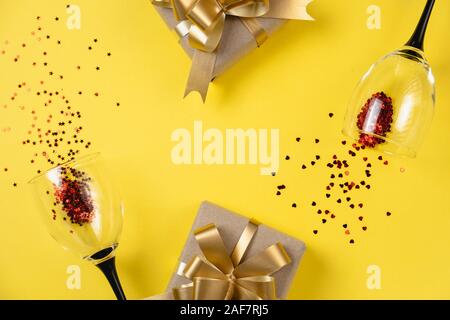 Holiday background. Two clinking wine glasses, various handmade gift boxes decorated with red heart confetti on yellow background. Valentines day conc Stock Photo