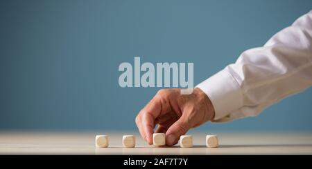 Hand of a businessman placing five blank wooden dices in a row on wooden desk. Over blue background with copy space. Stock Photo