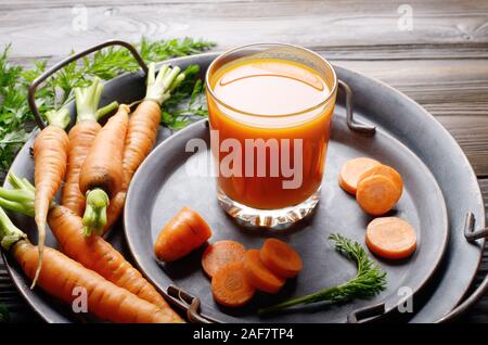 Vegetarian background of old fashioned tray with fresh organic carrots and juice on kitchen wooden table Stock Photo