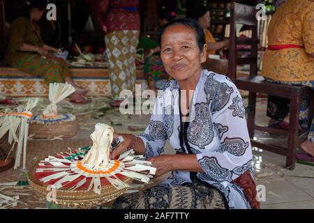 Smiling Balinese woman in a batik dress making flower offerings to the Gods at a Hindu temple Stock Photo