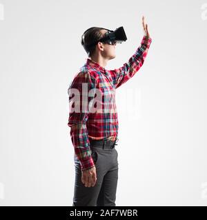 Young man in checked shirt wearing virtual helmet against gray background Stock Photo