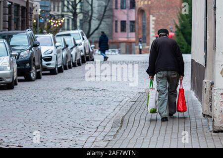 Along the paved streets of the old town go old man with bags. Rear view - image Stock Photo