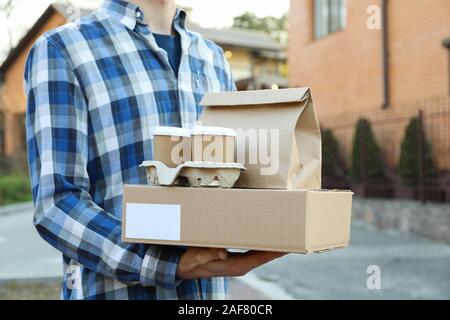 Man holds blank box, coffee cups and paper package outdoor. Delivery Stock Photo