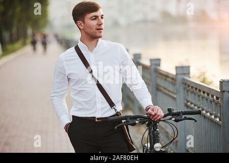 Focused photo. Businessman in formal clothes with black bicycle is in the city Stock Photo