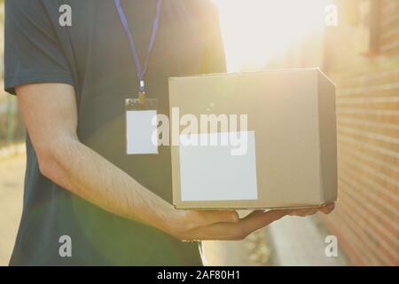 Delivery man with badge holds blank box outdoor, space for text Stock Photo