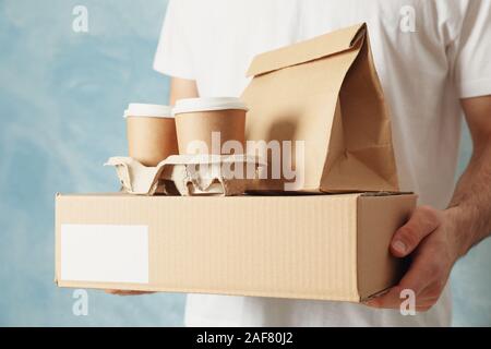 Man holds blank box, coffee cups and paper package indoor, space for text Stock Photo