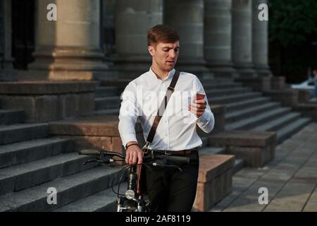 Need to call a general manager. Businessman in formal clothes with black bicycle is in the city Stock Photo