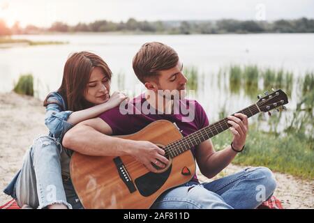 Man plays guitar for his girlfriend at beach on their picnic at daytime Stock Photo