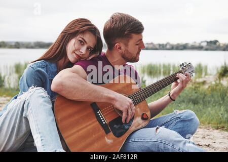 Nice skills. Man plays guitar for his girlfriend at beach on their picnic at daytime Stock Photo
