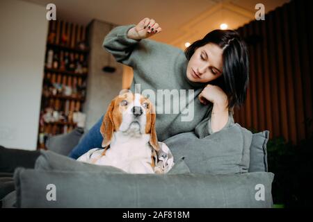 A woman lies on a sofa next to a beagle dog and plays with him.