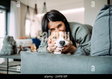 A woman lies on a sofa next to a beagle dog and hugs him.