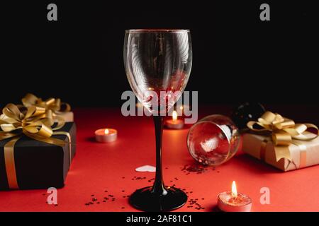 Holiday background. Two clinking wine glasses, various handmade gift boxes decorated with confetti, candle on red and black background. Valentines day Stock Photo