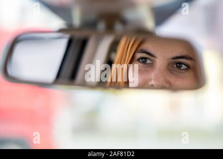 Young woman driver checking rear view mirror looking backwards while driving a car. Stock Photo