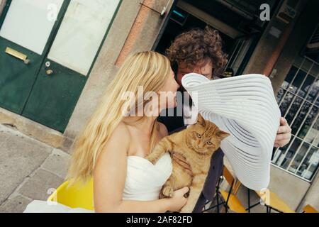 Loving wedding couple sitting in a cafe on the street with a red cat Stock Photo