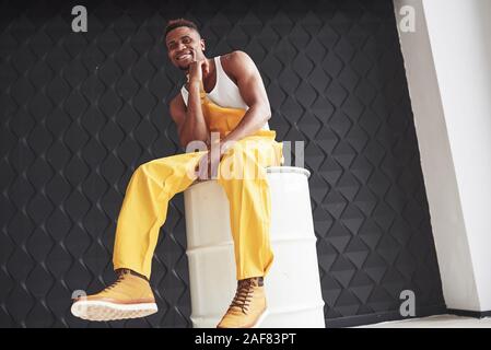 Using barrel as chair. Young african american worker in the yellow uniform have some job Stock Photo