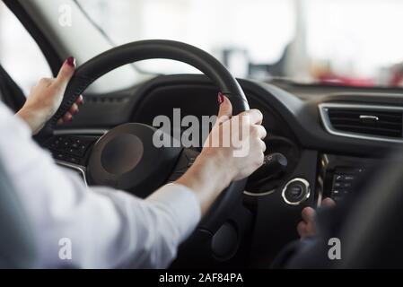 Hands on steering wheel. Woman in official clothes trying her new car in automobile salon Stock Photo