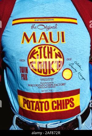 A man wears a blue shirt that replicates the front of an actual package of Maui Potato Chips, a famous snack made in Maui since 1956 that is known throughout the Hawaiian Islands, USA.  Although other makers now call their brands 'Maui' potato chips, the original product is identified by its red and yellow label and round 'Kitch'n Cook'd' logo. The 'Do Not Expose To Sunshine' warning is because the chips are packaged in clear plastic bags and the sun's UV rays and heat will cause the chips to go soft and taste stale since no chemical preservatives are used. Stock Photo