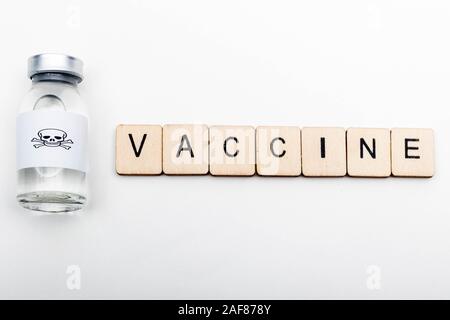 A glass medical vial with a skull and crossbones on a white background with a sign reading Vaccine Stock Photo
