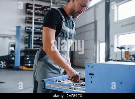 Different sizes. Male mechanic use different tools to repair broken automobile in garage Stock Photo