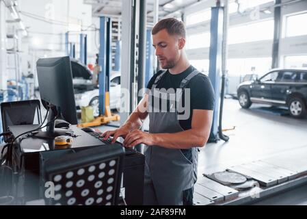 Typing on keyboard. Man at the workshop in uniform use computer for his job for fixing broken car Stock Photo