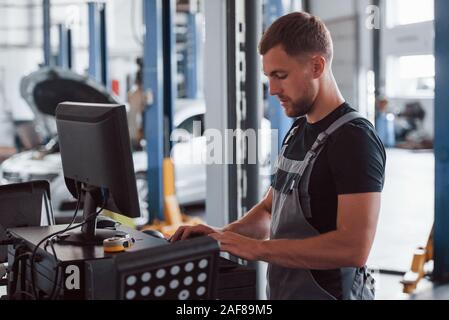 Professional mechanic. Man at the workshop in uniform use computer for his job for fixing broken car Stock Photo