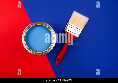 Brush with black handle on open can of teal paint on blue pastel background. Color of the year in interior. Stock Photo
