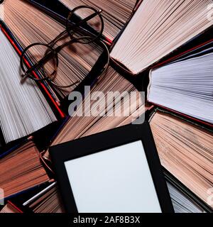 The e-book with a white screen lies on the open multi-colored books that lie on a dark background, close-up Stock Photo