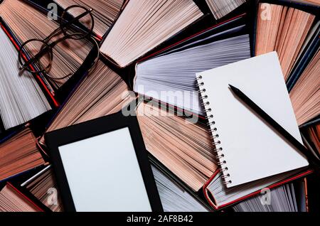 The e-book with a white screen lies on the open multi-colored books that lie on a dark background, close-up Stock Photo