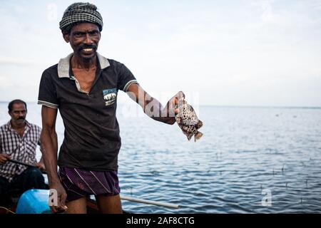 Vembanad lake, Kerala - 20 october 2019: portrait of an indian fisherman on a boat fishing and showing fish, a symbol of indian economy and food crisi Stock Photo
